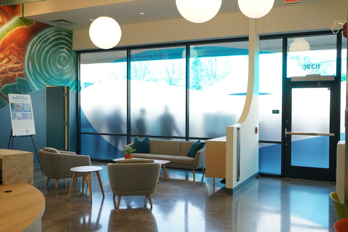 Lobby with frosted gladd windows, murals and stuffed chairs.