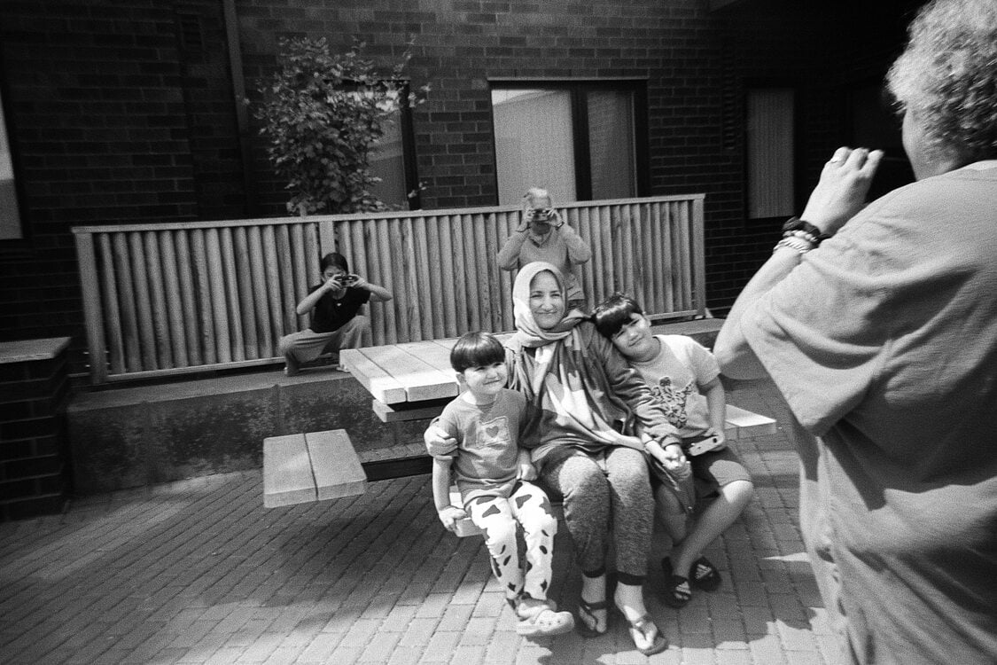 A group of people photographing each other with film cameras in an apartment building courtyard.