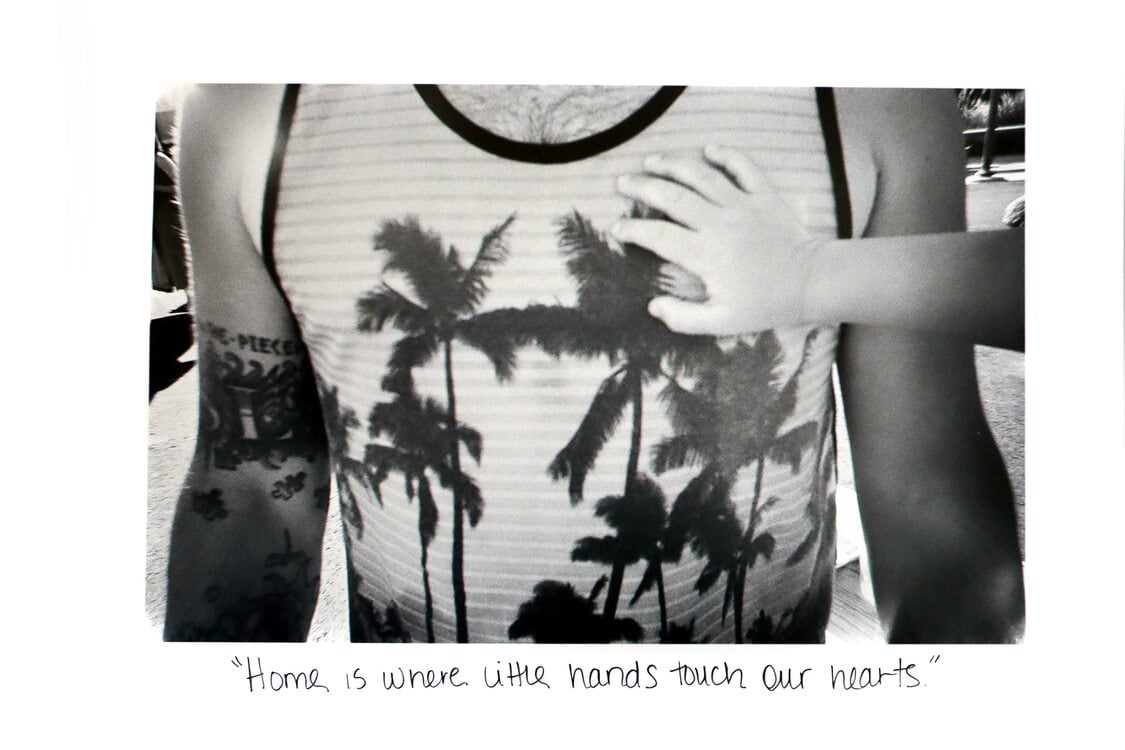 Black and white photo of a child's hand over the heart of an adult wearing a tank top with palm trees. 