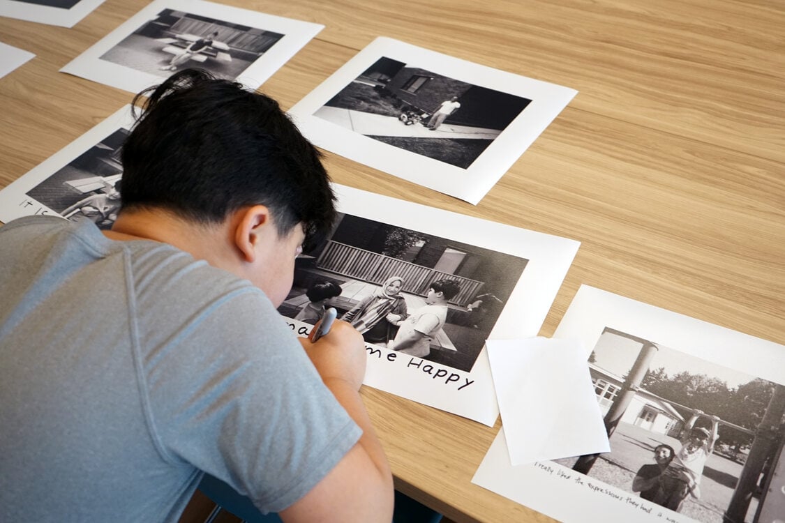 A young boy writes on a black and white photo print.