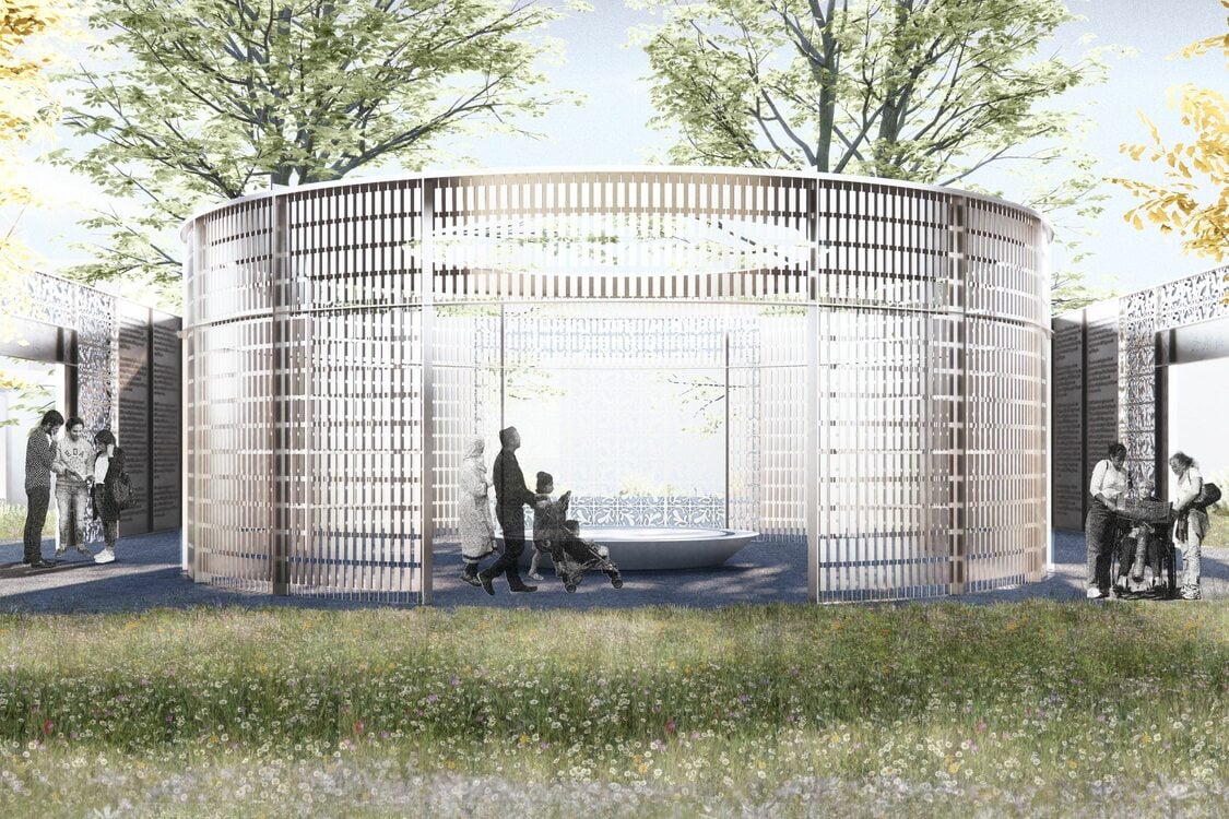 People stroll through an outdoor pavilion surrounded by trees and grass, some stopping to read informative plaques on the pavilion's stone walls