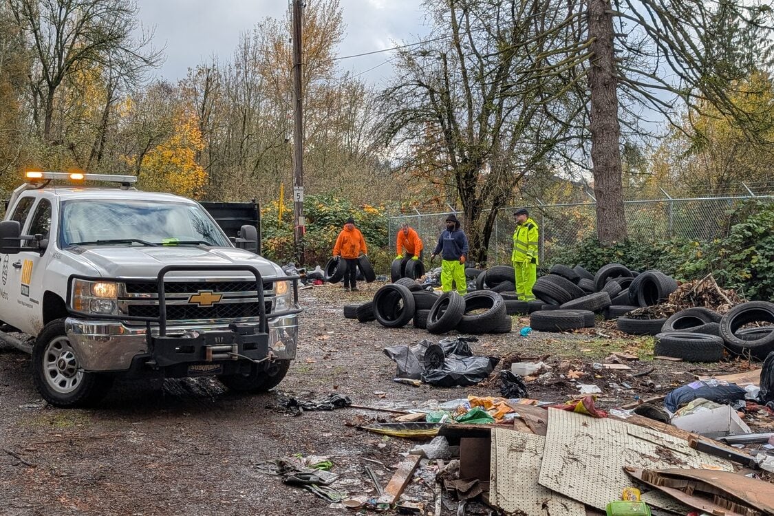 A wide-angle perspective of RID staff in high-visibility clothes at a worksite, loading a pile of tires into a work truck. 