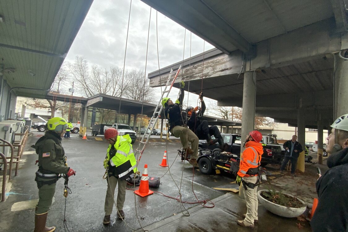 Several RID staff belay themselves from a parking lot overhang as practice. 