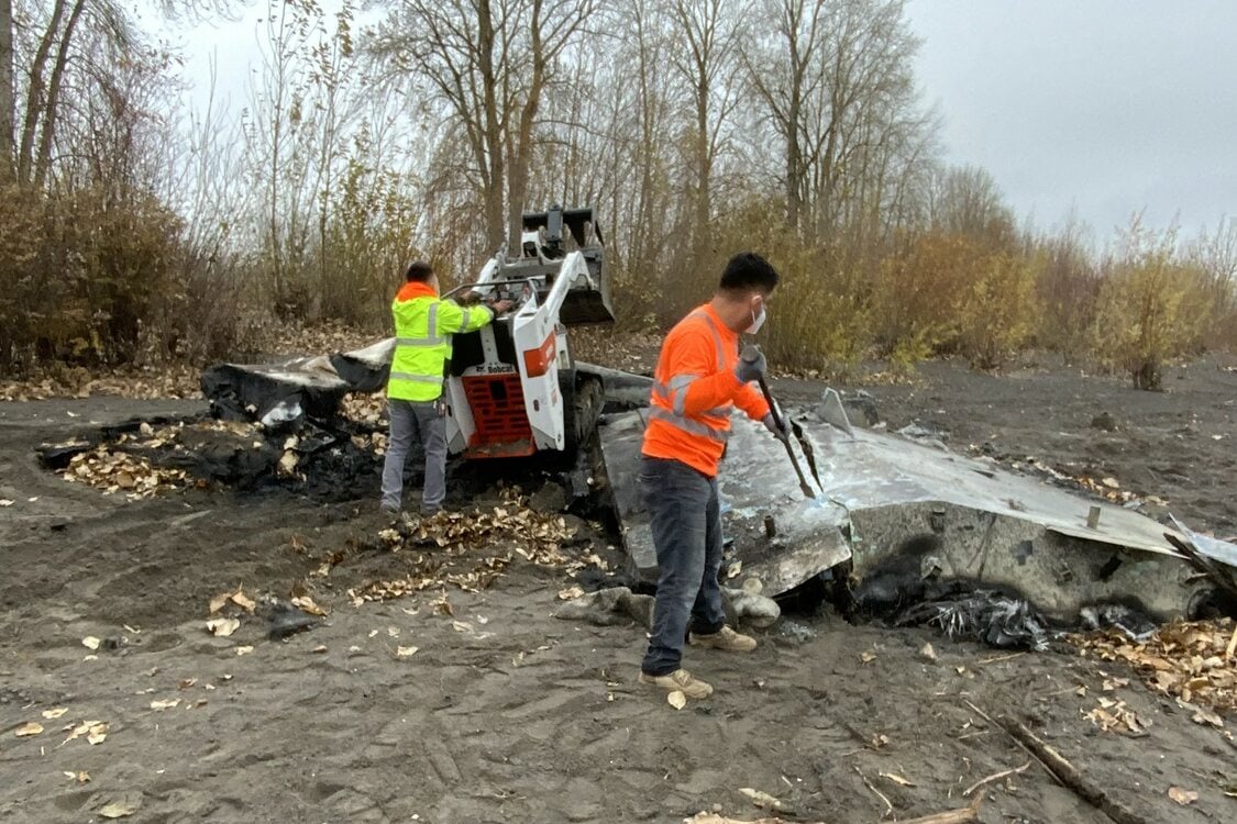 Two RID workers in high-visibility clothes work on clearing out charred scrap metal. 