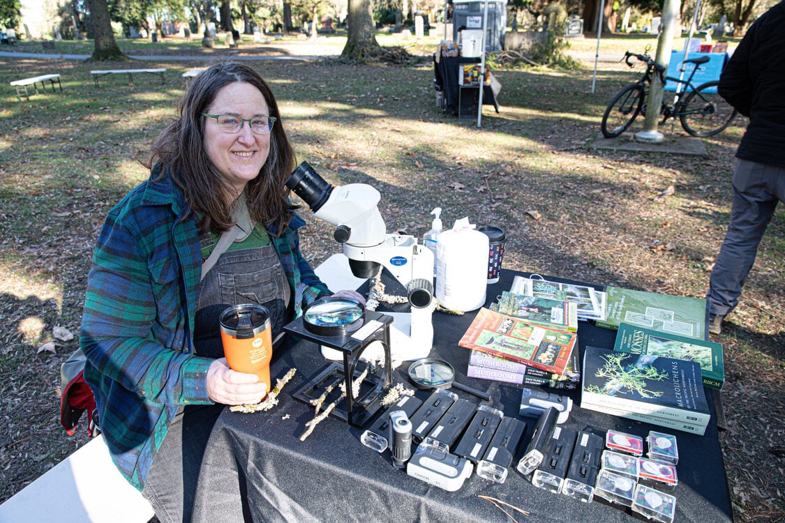 Bioblitz participant sits at a table of lichen books and a microscope to examine lichen.