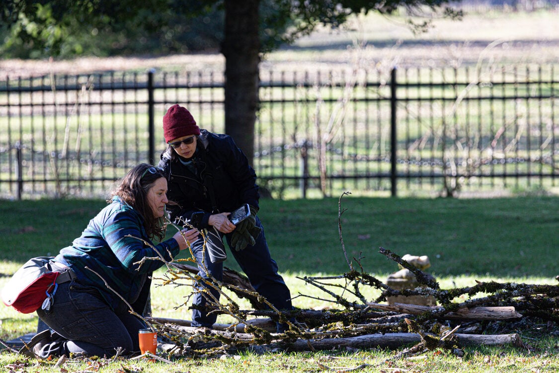 Two women observe lichen on branches on the ground at Lone Fir Cemetery during a bio blitz.