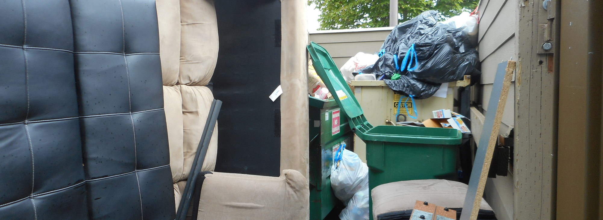 couch and other furniture in recycling area alongside recycling bins and dumpster