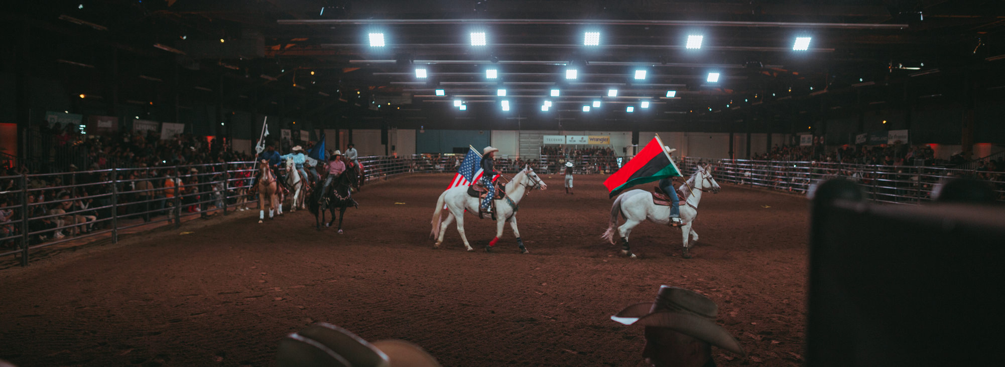 A group of rodeo participants ride their horses in a circle while carrying large flags from their home countries in the arena at Expo Center.