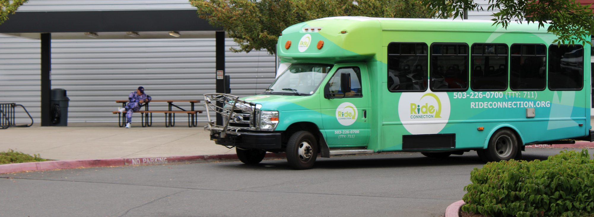 A Ride Connection shuttle bus, painted in shades of green with the Ride Connection logo prominently displayed on the front and sides of the shuttle bus.