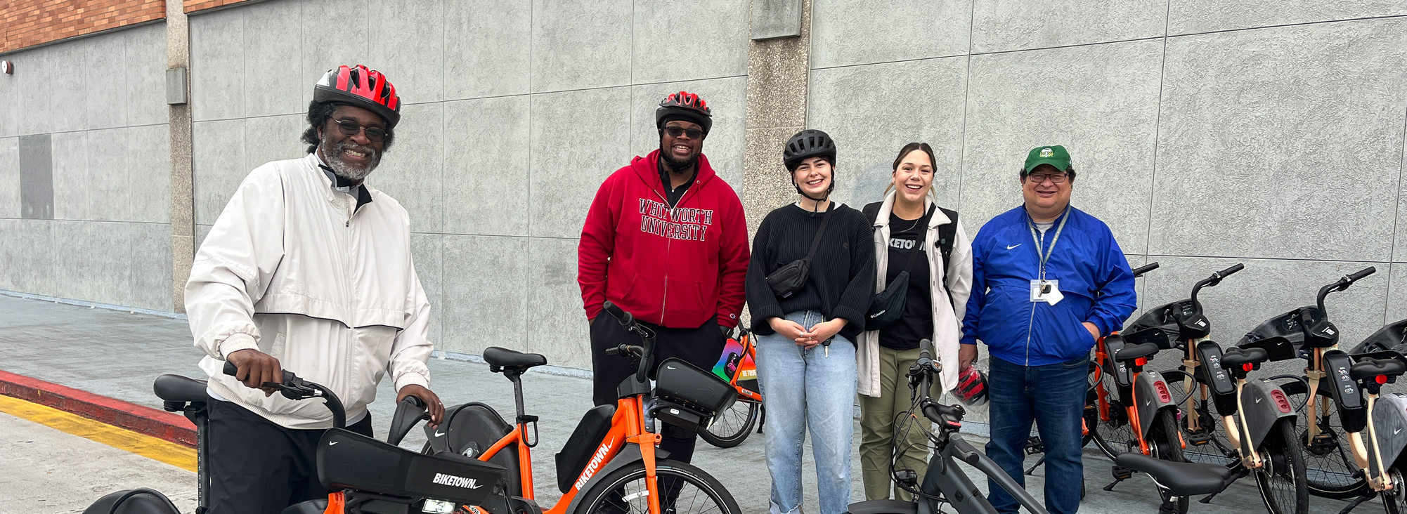 A group of adults with Community Street Trust smile at the camera, standing near a fleet of bicycles. 