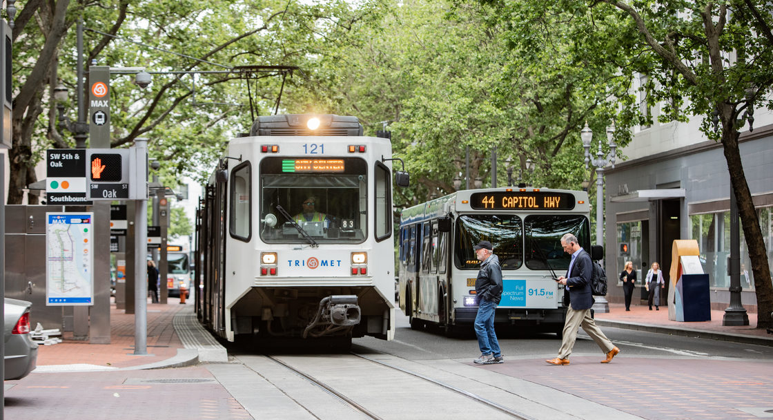 pedestrians cross in front of a MAX train and TriMet bus