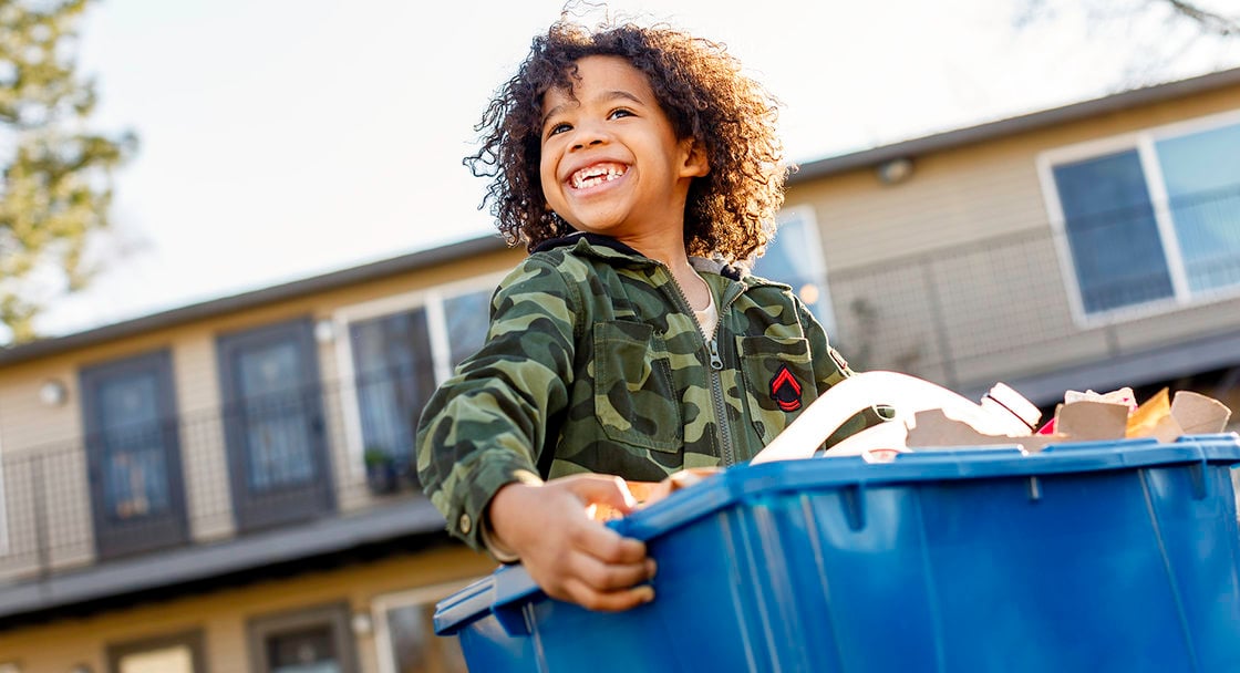 smiling child carrying a full recycling bin