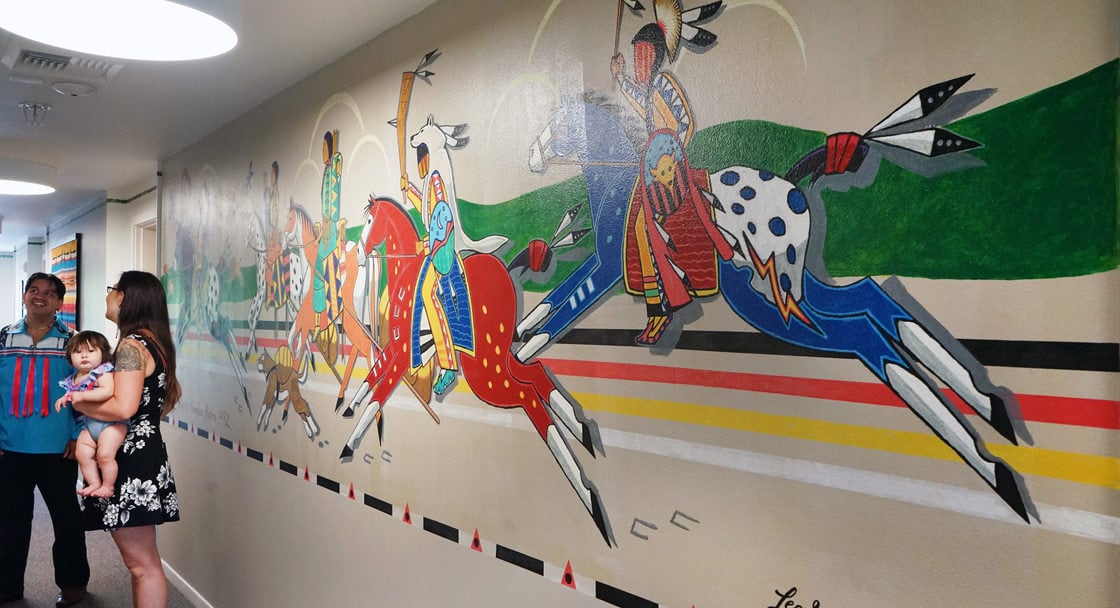 Large mural depicting Native Americans riding multicolored horses, with a man, woman and baby standing to the side chatting.