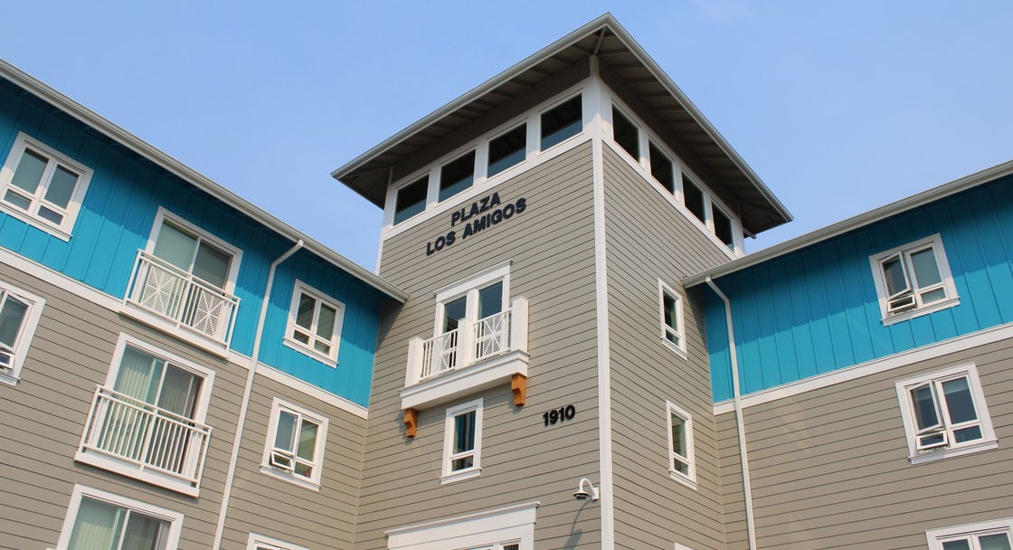 Exterior view of Plaza Los Amigos affordable housing project in Cornelius, a multistory building painted in shades of beige and bright blue.