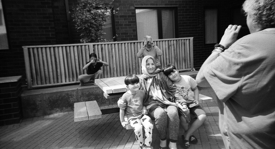 A group of people photographing each other with film cameras in an apartment building courtyard.