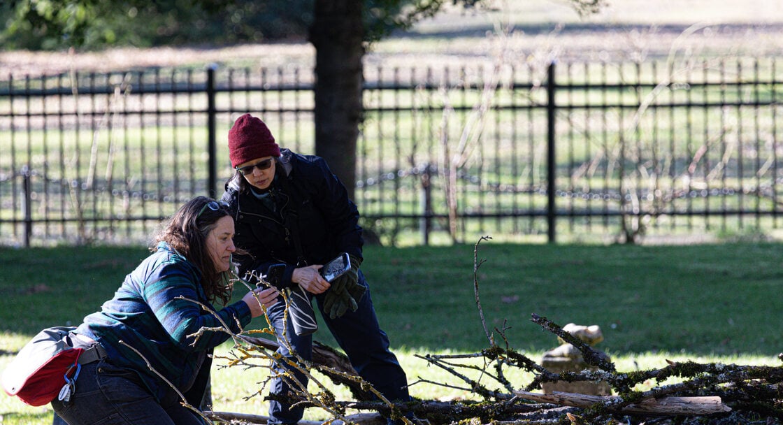 Two women observe lichen on branches on the ground at Lone Fir Cemetery during a bio blitz.