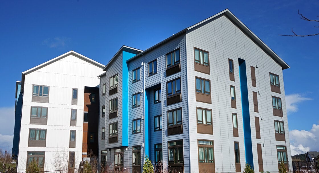 A four-story multifamily building with white, blue and grey exterior finish. 