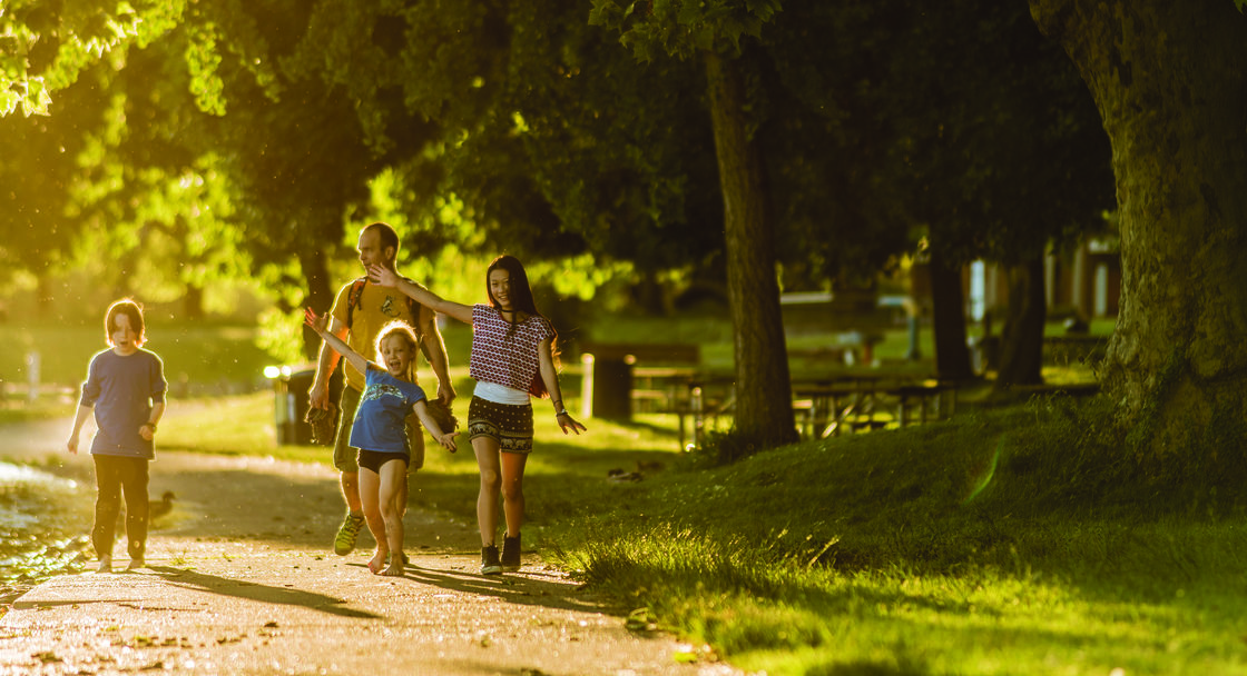 A family of four, including two young kids, walk along a tree-lined path at Blue Lake Regional Park.